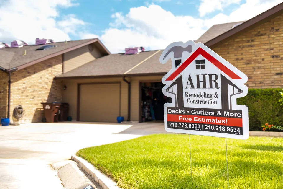 AHR Remodeling & Construction yard sign, listing decks and gutters, on the lawn of a home whose roof is being replaced.