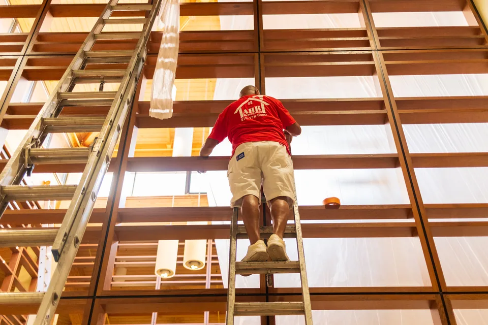 AHR crew member on a ladder, working high on the wood screens inside a commercial building.