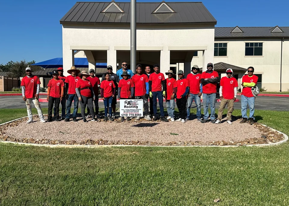 American Homes Roofing crew in red company shirts, lined up behind a company yard sign.